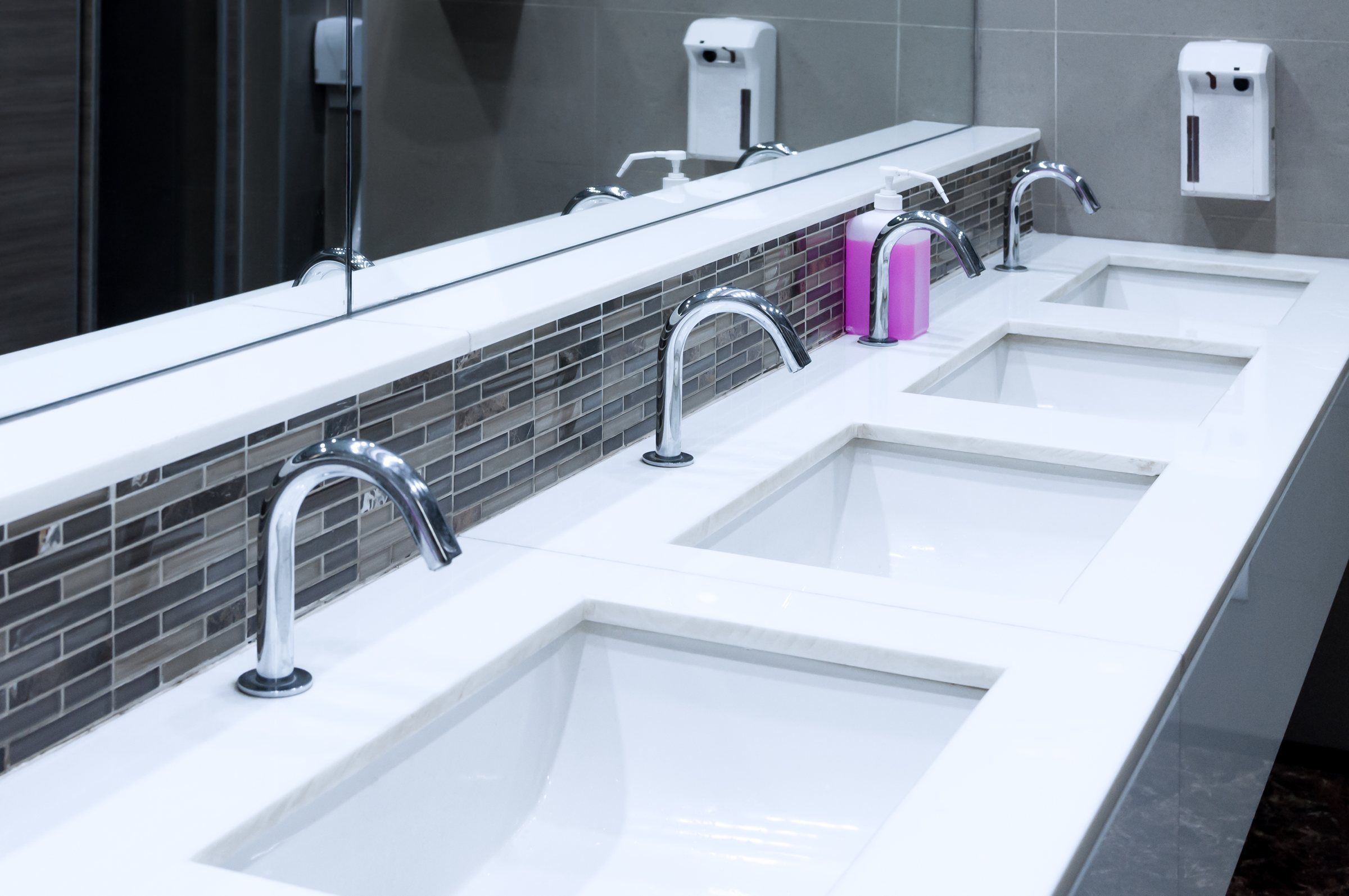 Row of commercial restroom sinks with sensor faucets