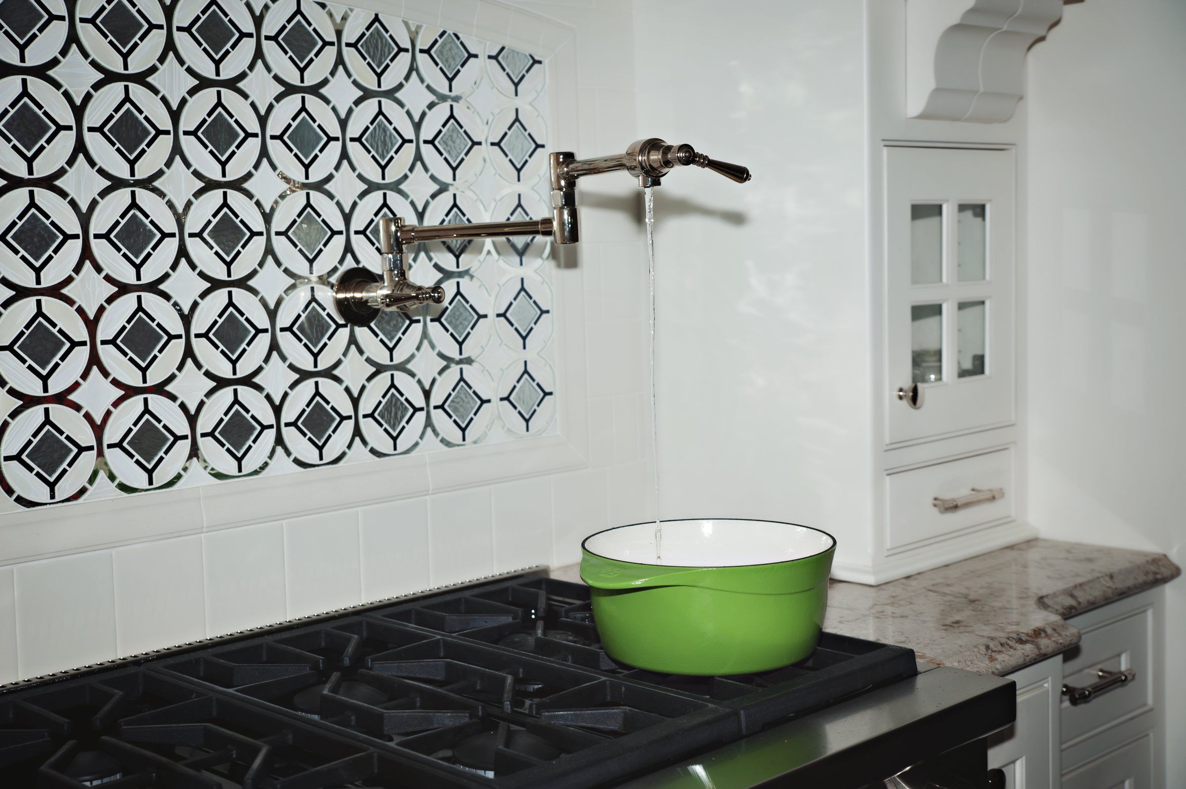 Wall-mounted pot filler faucet above a gas range with patterned tile backsplash