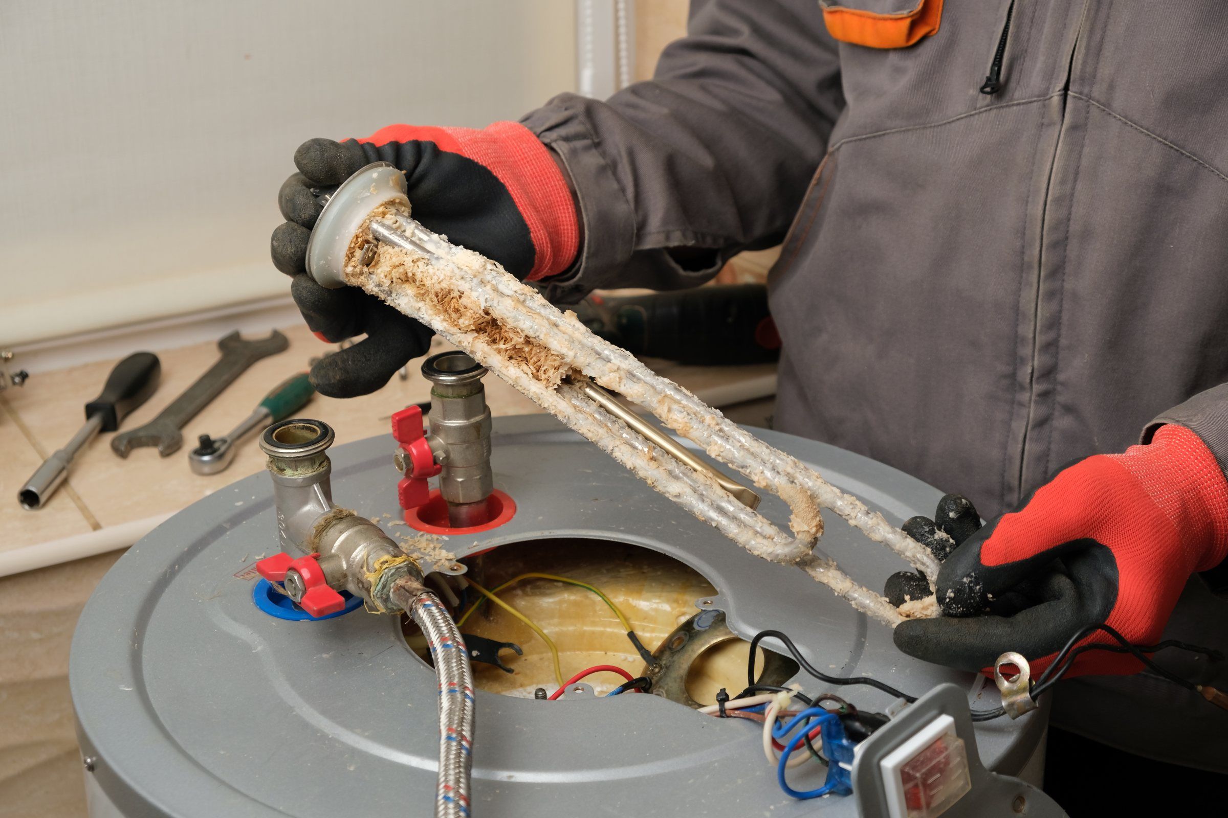 Plumber holding a water heater element heavily coated in mineral scale beside the opened tank